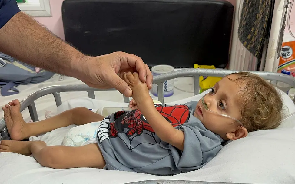 Gaza spenden: Ein Kleinkind wird im Krankenhaus beatmet und hält die Hand eines Mannes fest. 