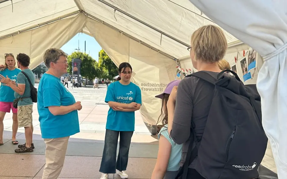In einem großen weißen Zelt stehen und sitzen Interessierte und nehmen an der Aktion zum Weltflüchtlingstag teil In einem großen weißen Zelt stehen und sitzen Interessierte und nehmen an der Aktion zum Weltflüchtlingstag teil