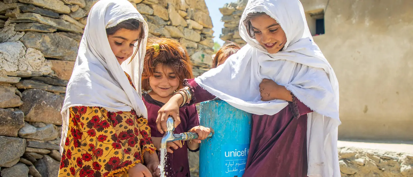 Kinder zapfen frisches Wasser an einem Zapfhahn.