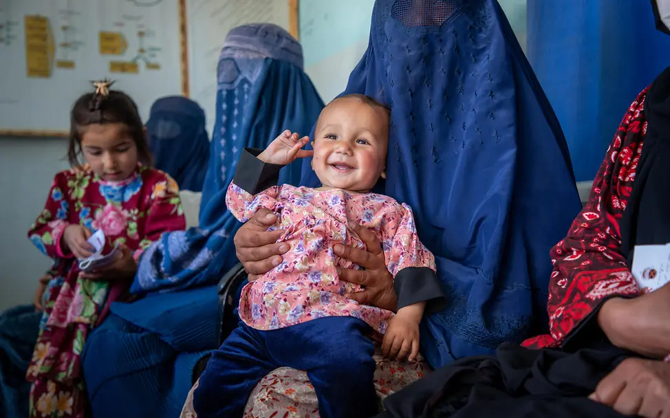 Ein breites Grinsen im Gesicht von Freshta. | © UNICEF/UNI777910/Azizi Ein Kind ist auf dem Arm der Mutter und lächelt glücklich.