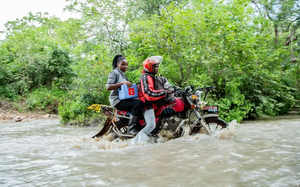 Warum impfen: Zwei Gesundheitshelfer transportieren Impfstoffe auf einem Motorrad durch einen Fluss.