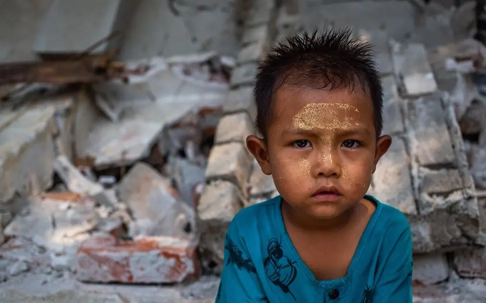 Shine Khant Ko (3) vor zerstörten Gebäuden nach dem Erdbeben. | © UNICEF/Htet Wie entstehen Erdbeben: Ein Kind sitzt vor zerstörten Gebäuden nach einem Erdbeben.