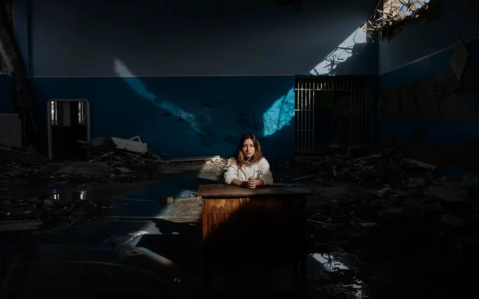 Daria (16) sitzt an einem Schreibtisch in der Turnhalle ihrer zerstörten Schule. | © UNICEF/Ibarra Sánchez Kinder im Krieg: Daria sitzt an einem Schreibtisch in der Turnhalle ihrer zerstörten Schule in der Ukraine.