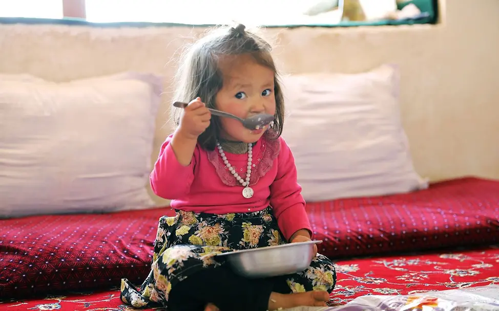 Kinderarmut spenden: Ein Mädchen in Afghanistan isst Reis und Gemüse aus einer Schüssel. 