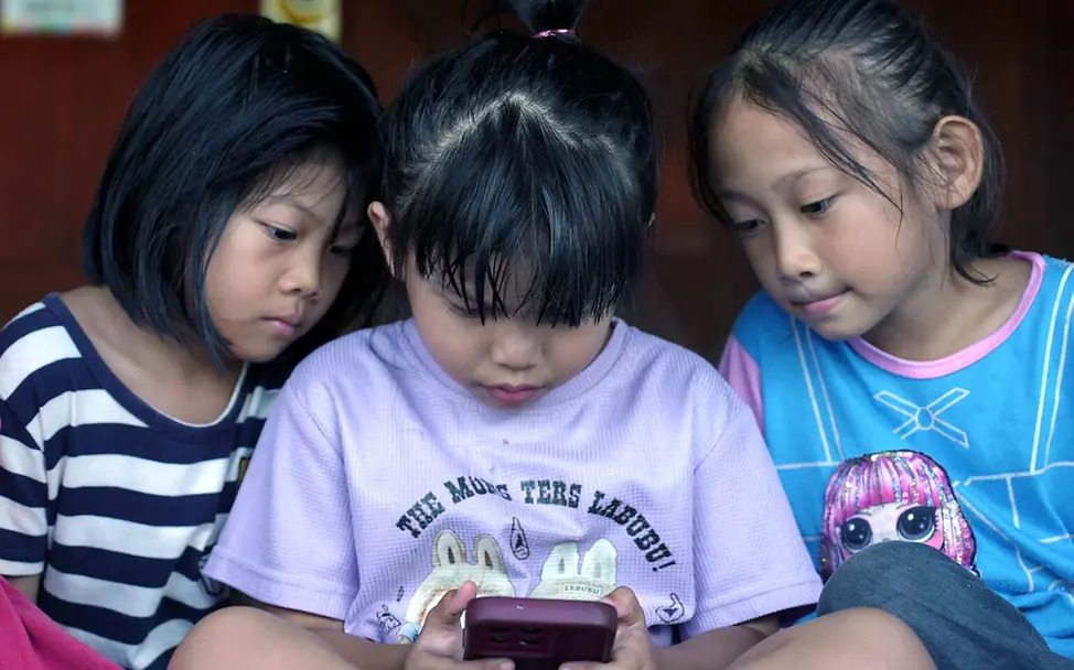 Drei Mädchen in Malaysia schauen zusammen auf ein Smartphone. | © UNICEF/Hazim Digitale Gewohnheiten: Drei Mädchen in Malaysia schauen zusammen auf ein Smartphone.