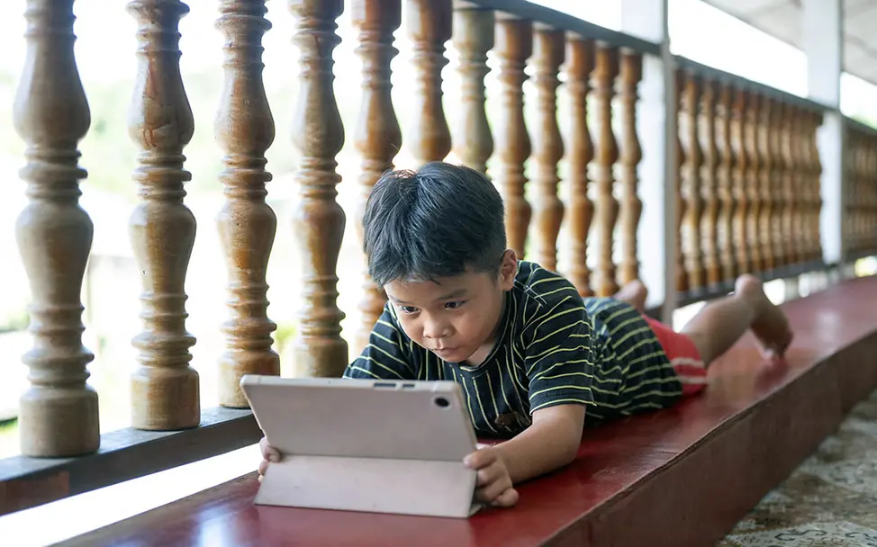 Ein Junge in Malaysia liegt auf dem Bauch und schaut auf ein Tablet. | © UNICEF/Sufari Digitale Gewohnheiten: Ein Junge in Malaysia liegt auf dem Bauch und schaut auf ein Tablet.