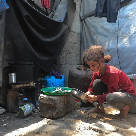 Tala (10) in einer Notunterkunft | UNICEF/Nateel Kinder in Gaza: Ein Mädchen sitzt an einer Kochstelle in einer Notunterkunft