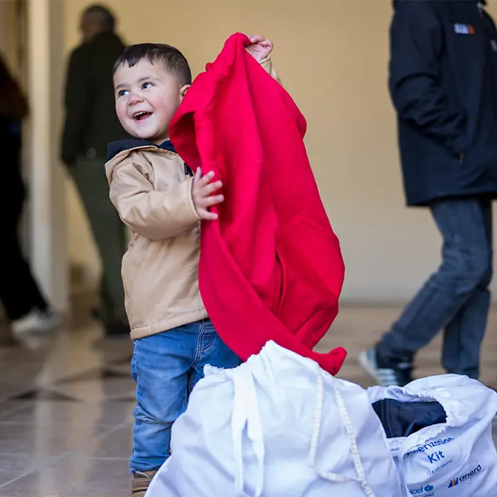 Ein Kind zieht eine Jacke aus einer Tüte voller Winterkleidung