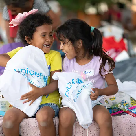 Originelle Geschenkideen für den guten Zweck: Zwei Mädchen packen lachend ihre UNICEF-Beutel aus.
