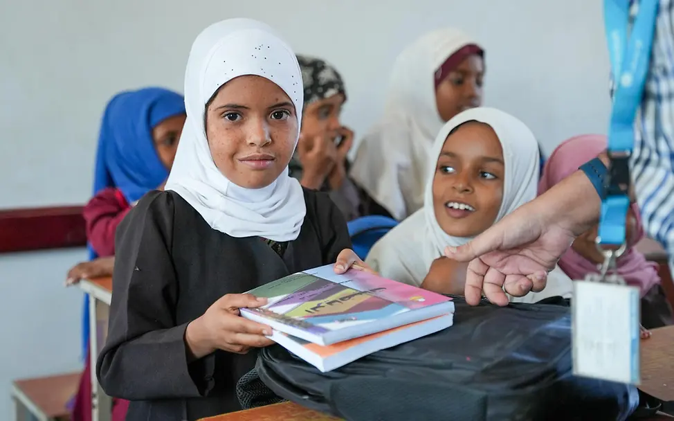Originelle Geschenkideen für den guten Zweck: Zwei Mädchen an einem Schultisch zeigen ihre neuen Bücher.