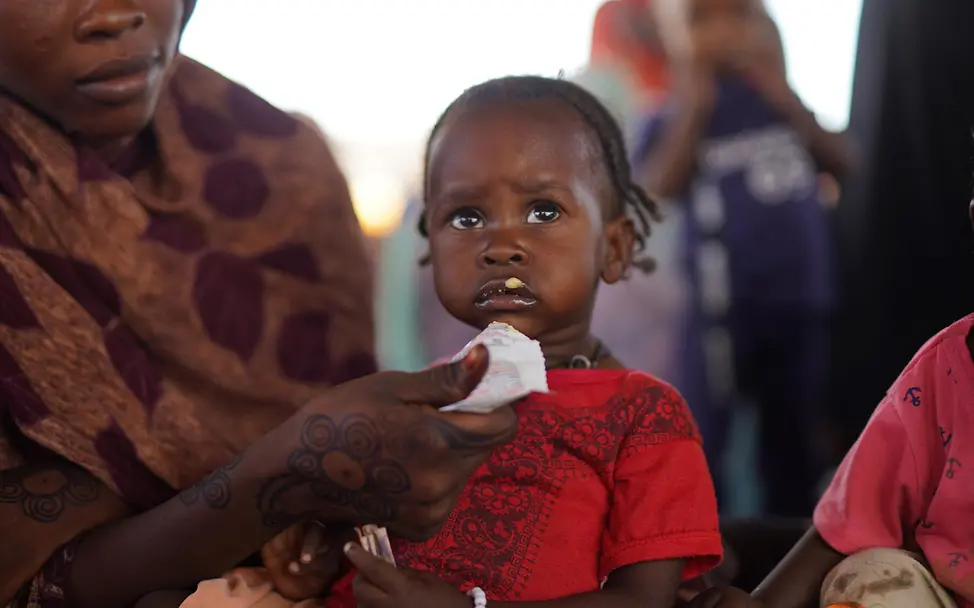 Originelle Geschenkideen für den guten Zweck: Eine Mutter füttert ihr Kind mit Erdnusspaste. 