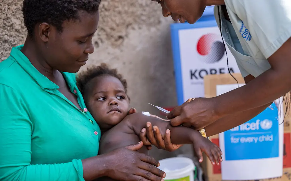 Originelle Geschenkideen für den guten Zweck: Eine UNICEF-Helferin impft ein Baby auf dem Schoß seiner Mutter. 