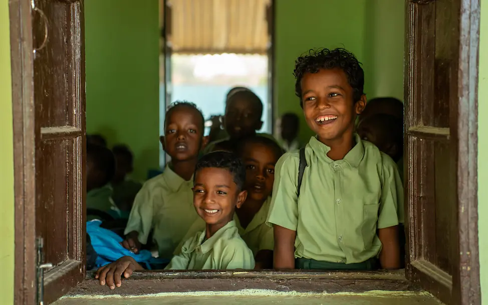 Originelle Geschenkideen für einen guten Zweck: Zwei Jungen schauen lächelnd aus dem Fenster ihrer Schule im Sudan. 