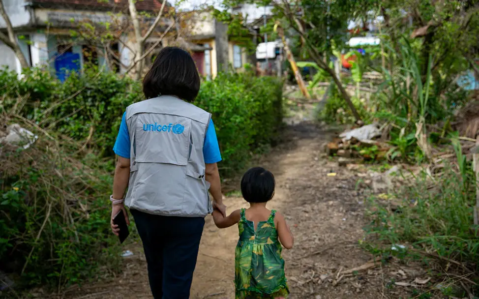 Originelle Geschenkideen für einen guten Zweck: Eine UNICEF-Helferin geht mit einem kleinen Mädchen an der Hand.