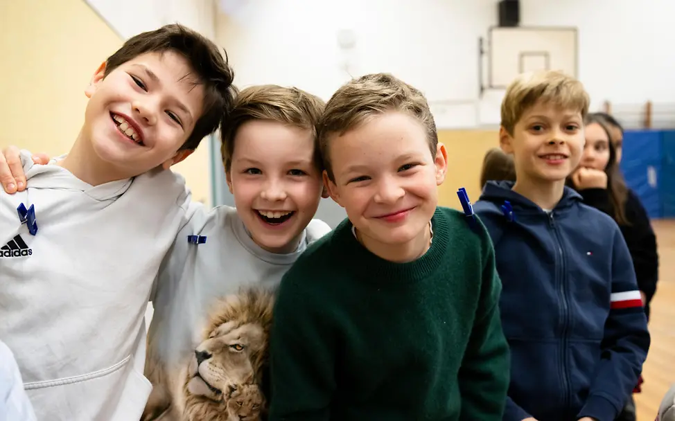 Originelle Geschenkideen für einen guten Zweck: Vier Jungen in einer Schulsporthalle lächeln in die Kamera.