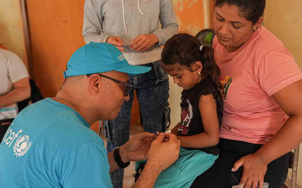 Ein UNICEF-Gesundheitshelfer in Venezuela versorgt ein auf dem Schoß ihrer Mutter sitzendes Mädchen. | © UNICEF/Pocaterra Venezuela Spenden Krise: Ein UNICEF-Gesundheitshelfer bereitet ein Mädchen auf seine Impfung vor.