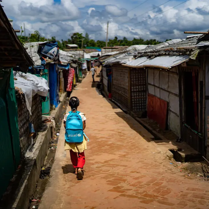 Rohingya in Bangladesch: Das Rohingya-Camp im Distrikt Cox’s Bazar ist das größte Lager weltweit. | © UNICEF Rohingya Flüchtlingslager: Ein Mädchen mit UNICEF-Schulrucksack läuft zwischen Hütten im Rohingya-Camp entlang.