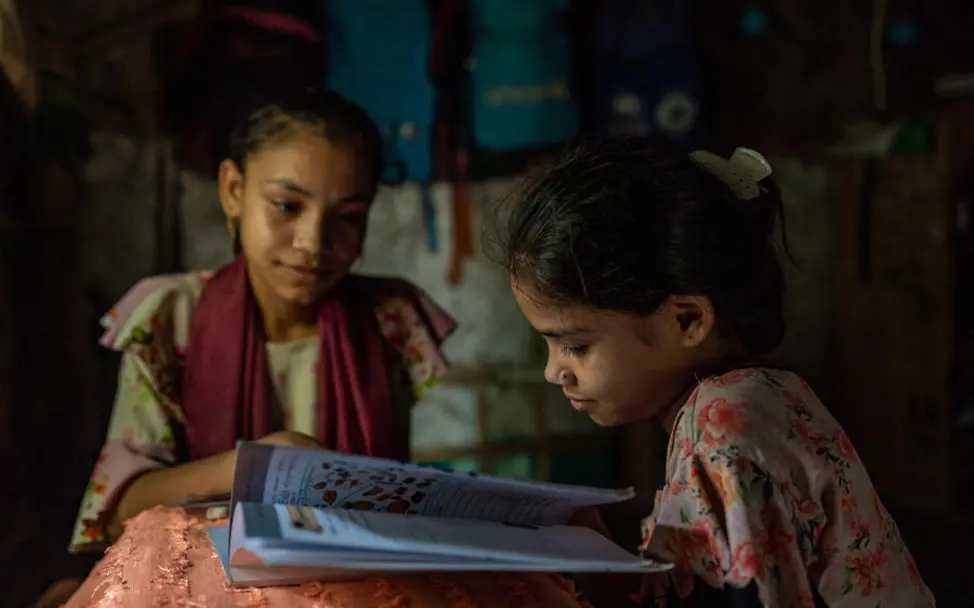 Rohingya in Bangladesch: Nicht alle Rohingya-Kinder in den Camps können regelmäßig zur Schule gehen. | © UNICEF Rohingya Flüchtlingslager: Zwei Mädchen sitzen mit einem Schulbuch in ihrer Unterkunft.
