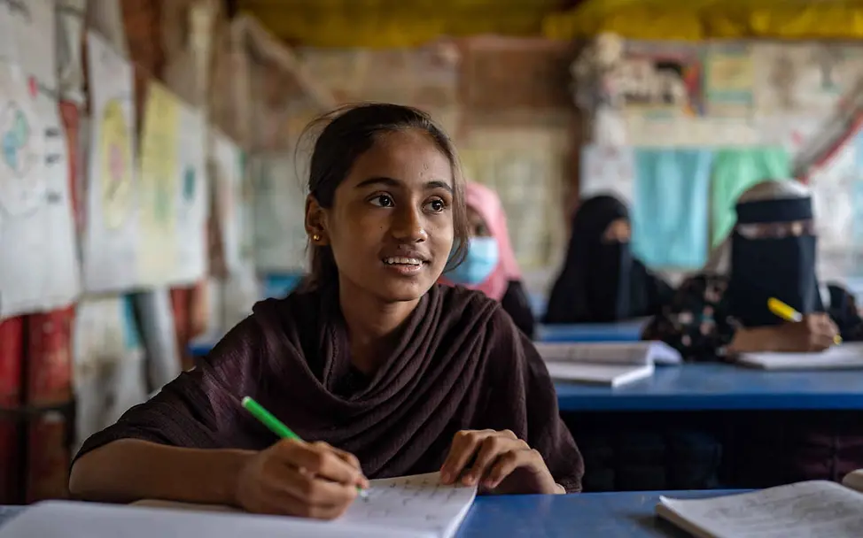 Rohingya in Bangladesch: UNICEF ist vor Ort, damit so viele Rohingya-Kinder wie möglich zur Schule gehen können. | © UNICEF Rohingya Flüchtlingslager: Ein Mädchen sitzt mit Schreibheft in der Schule.