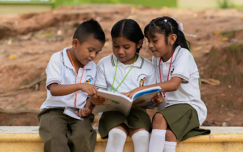 Kinderrechte leicht erklärt: Drei Schulkinder schauen ein Buch an.