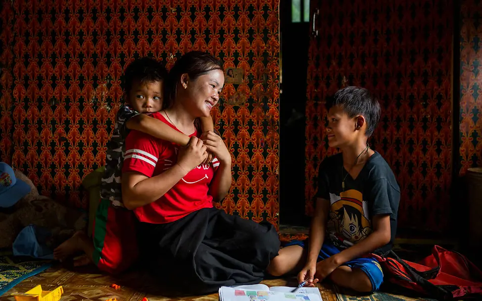 Menschenrechte einfach erklärt: Menschen haben ein Recht auf ein eigenes Zuhause. Menschenrechte einfach erklärt: Eine Mutter sitzt mit ihren zwei Kindern auf dem Boden ihres Hauses.