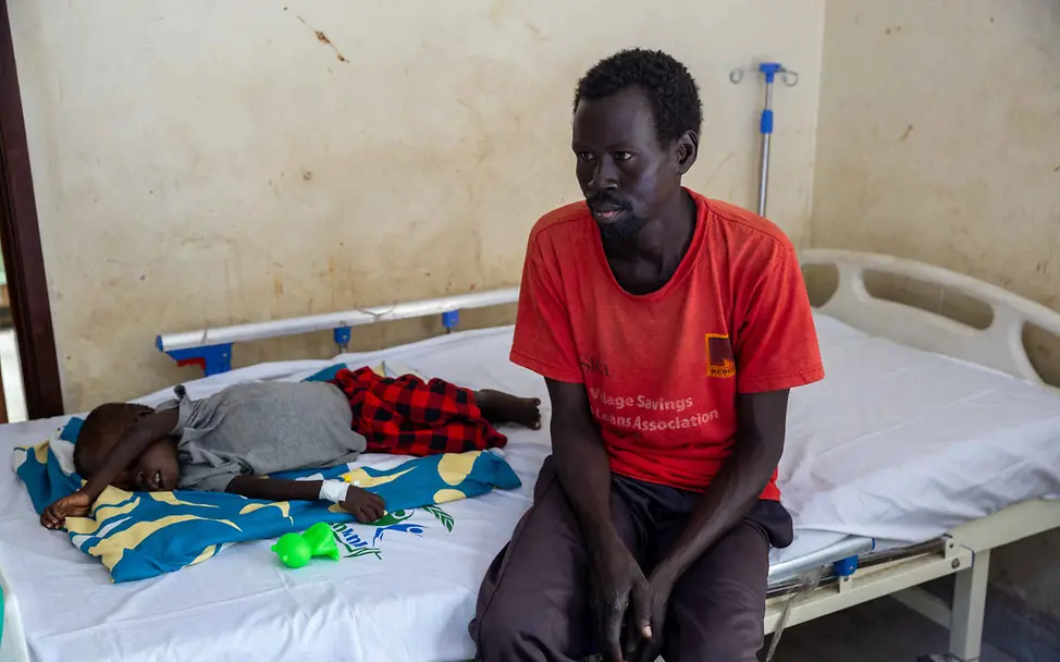 Hunger im Südsudan: UNICEF unterstützt die medizinische Versorgung von Kindern und ihren Familien. | © UNICEF/Prinsloo Südsudan Hungerkrise: Ein Vater sitzt bei seinem Kind auf einem Krankenhausbett.