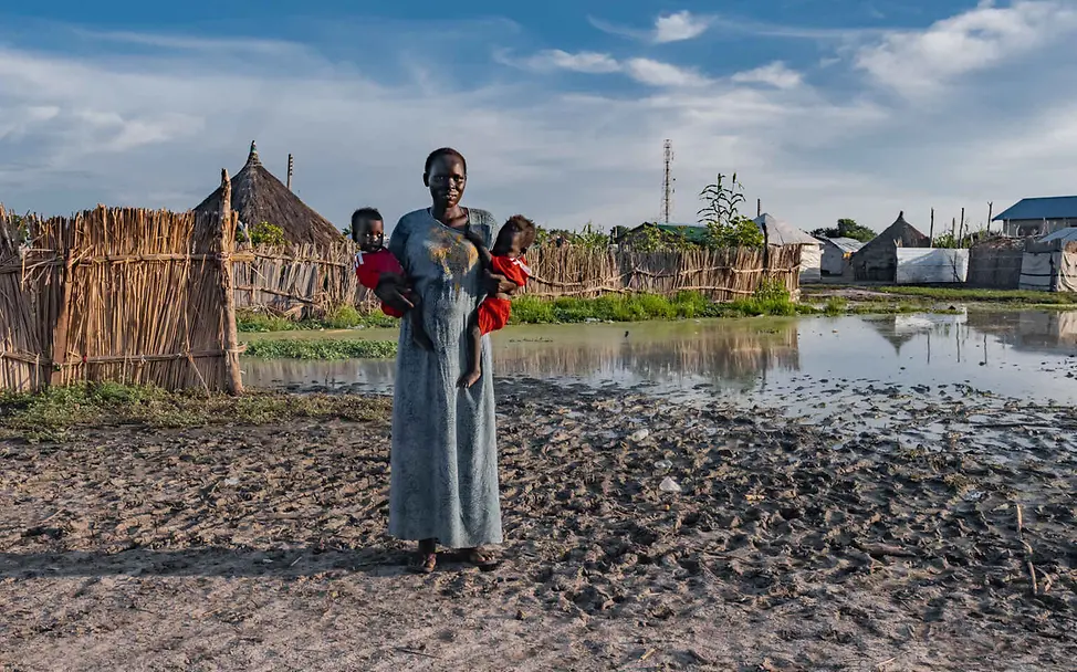 Hunger im Südsudan: In vielen Gebieten haben Überschwemmungen Dörfer und Ernten zerstört. | © UNICEF Südsudan Hungerkrise: Eine Mutter mit Zwillingen steht in ihrem überfluteten Dorf.