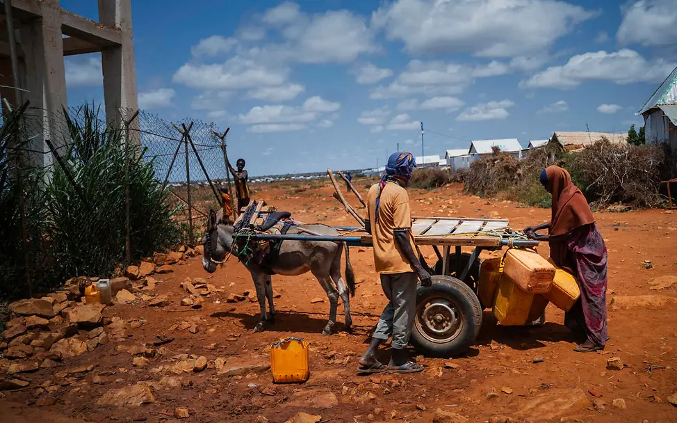 Was ist Klimaschutz: Hitze und Dürre führen in vielen Regionen der Welt zu Wassermangel. | © UNICEF/Fadhaye Klimaschutz einfach erklärt: In einer vertrockneten Landschaft laden zwei Menschen Wasserkanister auf einen Wagen.