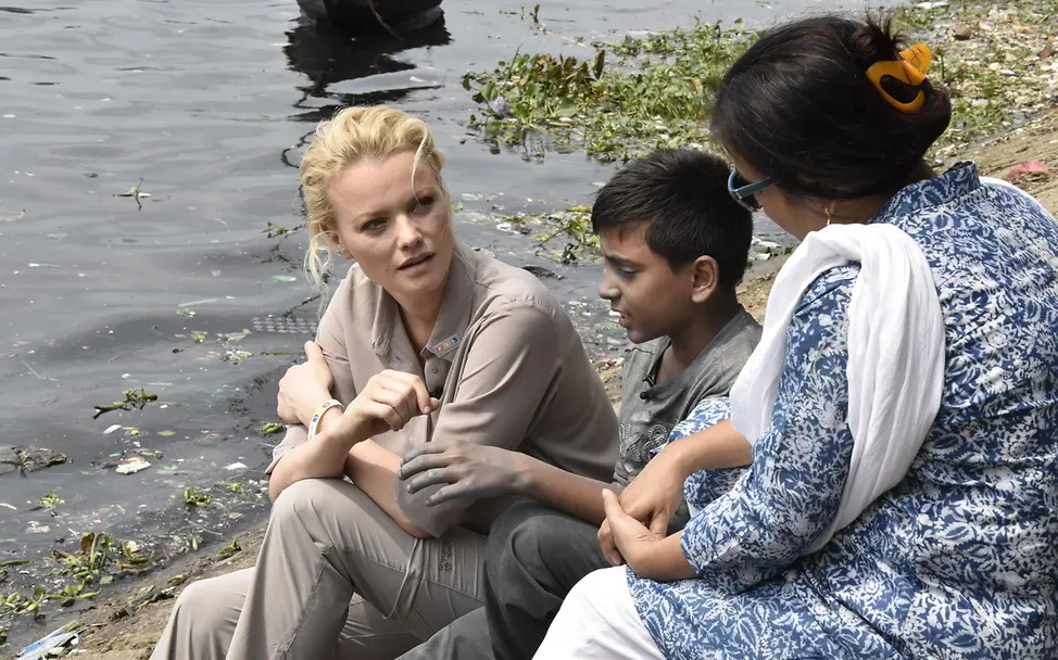 Franziska Knuppe im Gespräch mit Sumon | © UNICEF/UNI277648/Berger Drei Personen im Gespräch an einem Fluss
