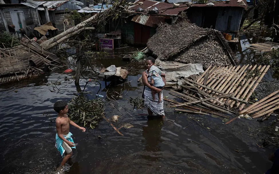 Wasserknappheit weltweit: Eine Frau und ihr Baby stehen im Wasser vor ihrem zerstörten Haus.