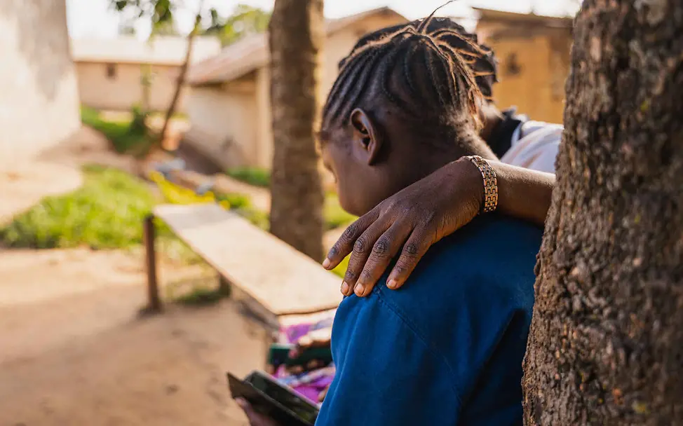 Kindersoldaten im Kongo: Ein Mädchen liest in einem Buch, eine Frau legt den Arm um sie.