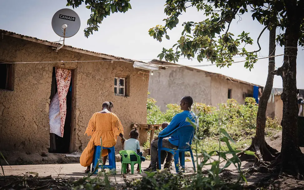 Kriegskinder im Kongo: Ein kleines Mädchen sitzt im Freien auf einem Stuhl zwischen seinen Eltern.