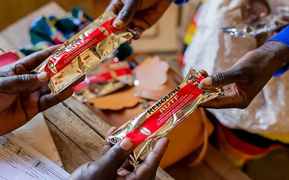 Zwei kleine silberne Päckchen mit lebensrettender Spezialnahrung (Erdnusspaste) werden übergeben