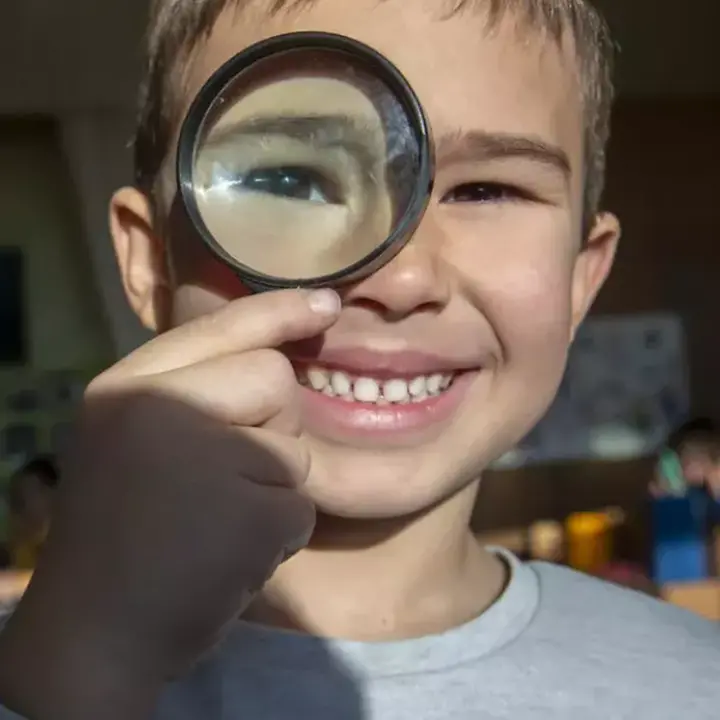 Junge hält sich eine Lupe vor das Gesicht.