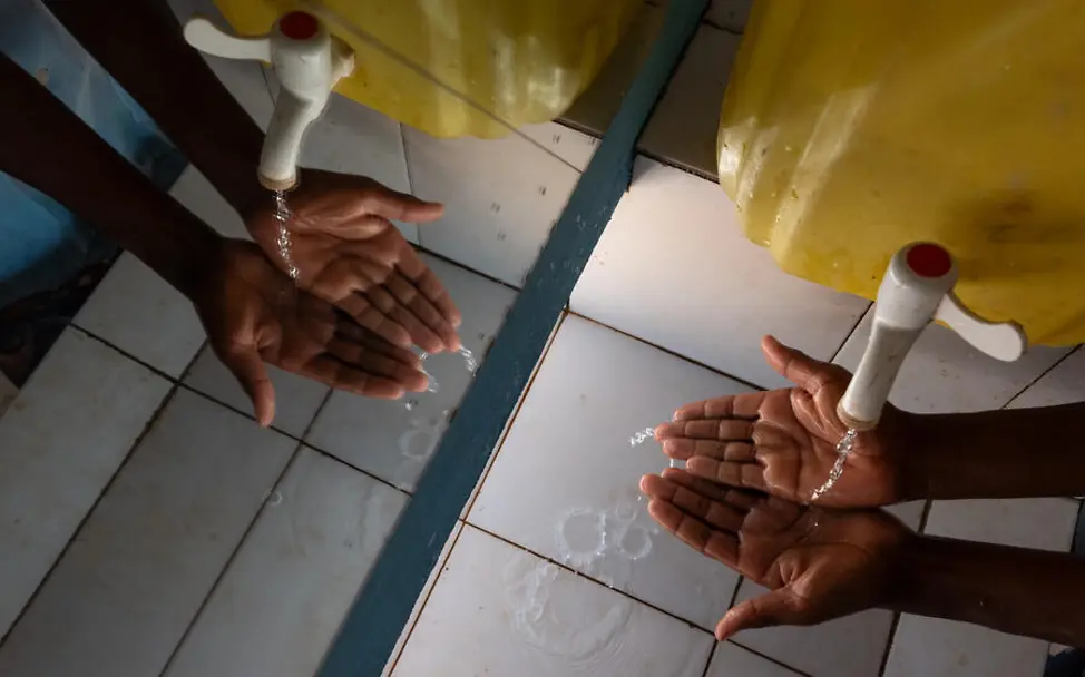 Was ist Periodenarmut: Zwei Hände, die sich die an einem Wasserkanister waschen. 