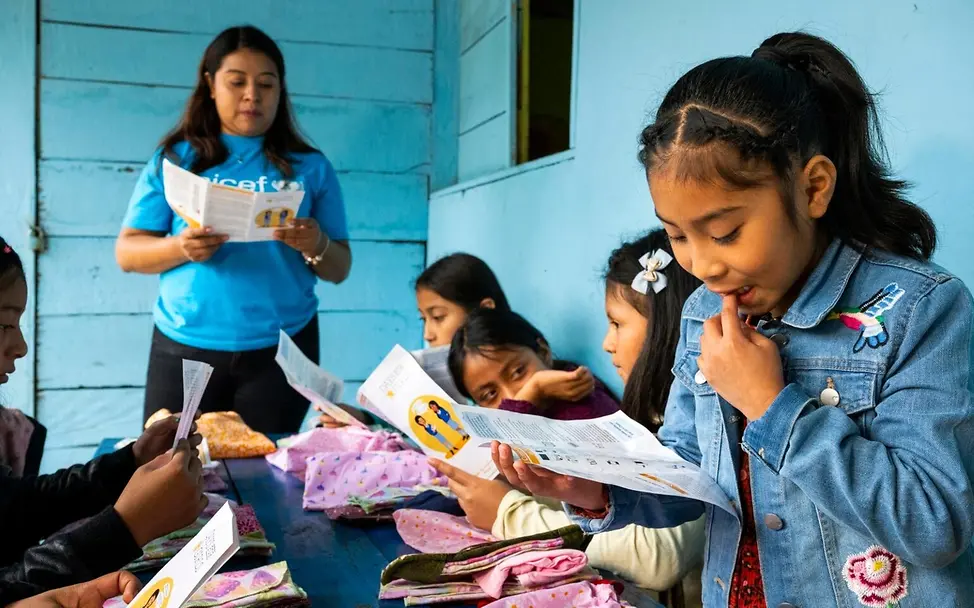 Was ist Periodenarmut: Mädchen und ihre Lehrerin schauen sich Menstruations-Sets an.