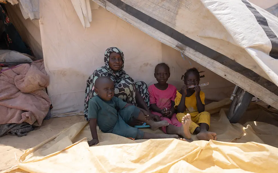 Eine Frau und drei Kinder sitzen im Schatten eines Zeltes.