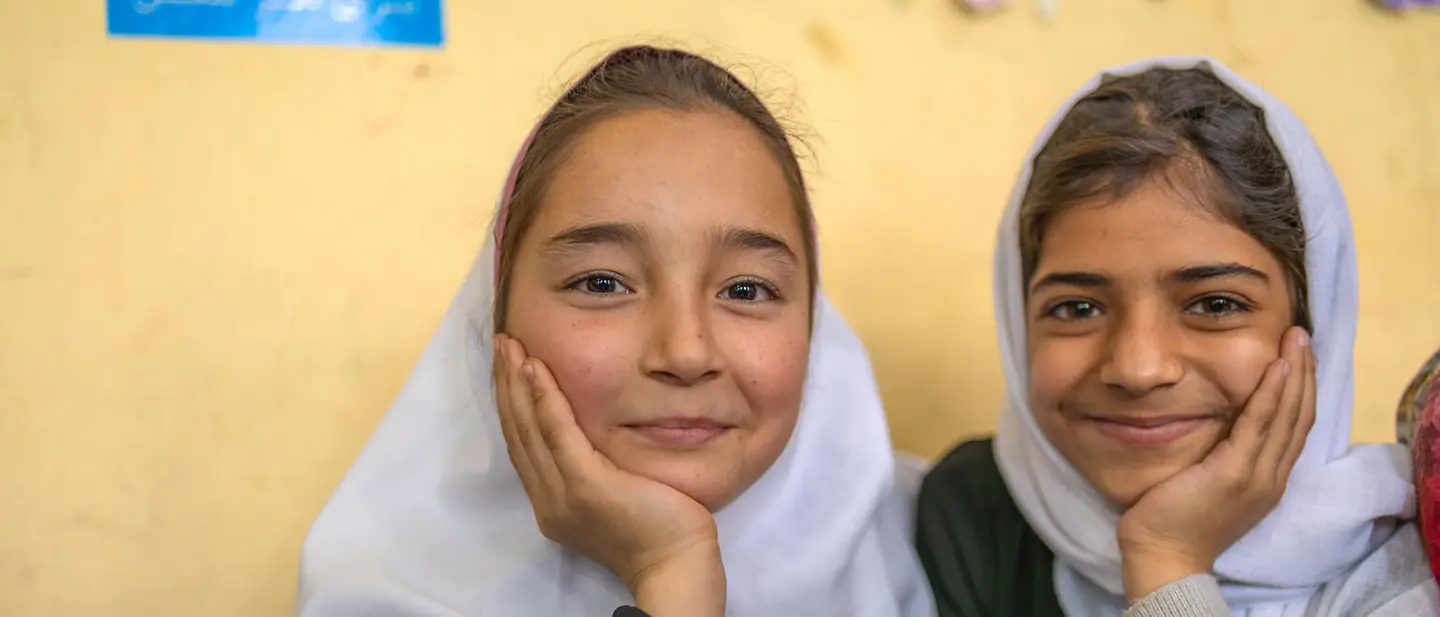Spenden für Mädchen: Zwei Mädchen in Afghanistan sitzen lächelnd in einem Klassenzimmer. 