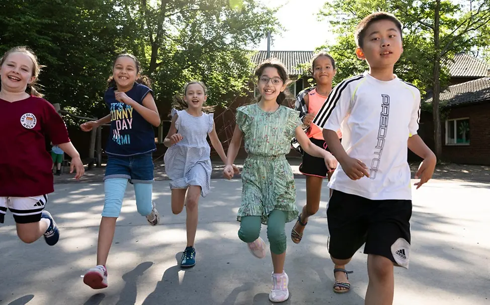 Grundgesetz einfach erklärt: Kinder auf einem Schulhof laufen lachend auf die Kamera zu. 