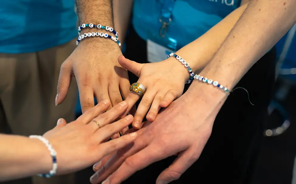Grundgesetz einfach erklärt: Vier Hände mit Namens-Armbändern berühren sich.