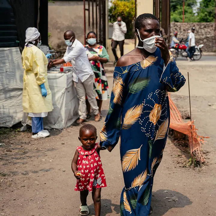 Eine Frau mit Atemschutzmaske geht mit ihrem Kind an der Hand an einer Gesundheitsstation im Kongo vorbei. | © UNICEF/AFP Ebola Kongo spenden: Eine Frau mit Atemschutzmaske geht mit ihrem Kind an der Hand an einer Gesundheitsstation im Kongo vorbei.