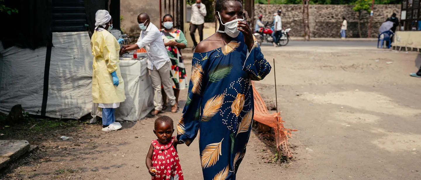 Ebola Kongo spenden: Eine Frau mit Atemschutzmaske geht mit ihrem Kind an der Hand an einer Gesundheitsstation im Kongo vorbei. 