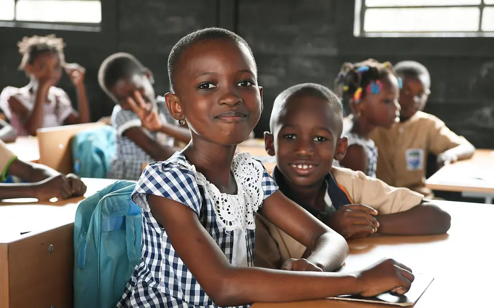 Bildung für die Elfenbeinküste: Schulkinder in einer Schule aus Recycling-Ziegeln lächeln in die Kamera. 