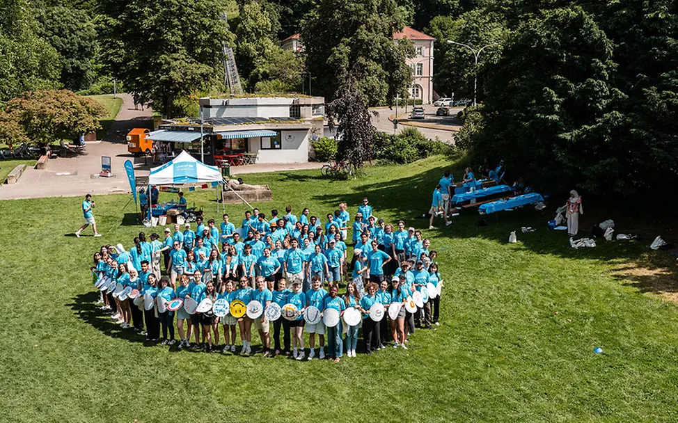 Freiwilligenarbeit junge Erwachsene: Viele junge Erwachsene mit UNICEF-Shirts stehen im Kreis auf einer Wiese. 