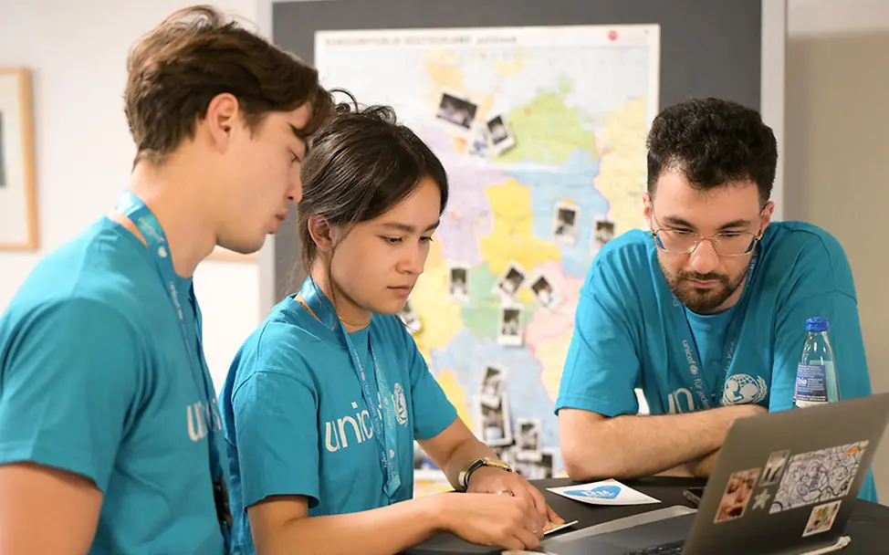 3 UNICEF-Engagierte stehen an einem Tisch und schauen gemeinsam auf einen Laptop. 