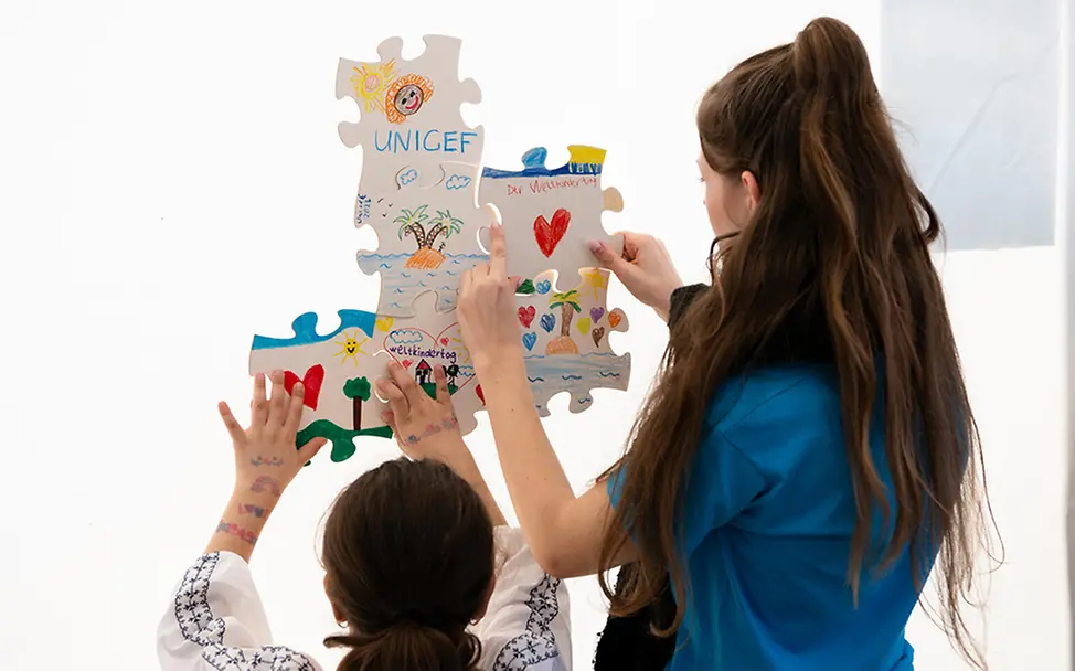 Freiwilligenarbeit junge Erwachsene: eine junge Freiwillige und ein Mädchen hängen ein Bild auf. 