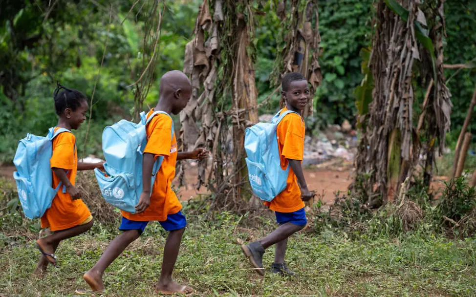 Kinderarbeit einfach erklärt: Drei Kinder mit UNICEF-Schulrucksäcken auf dem Weg zur Schule. 