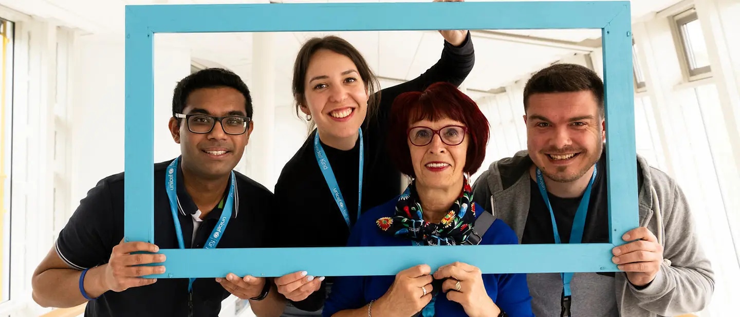 Ehrenamtlich aktiv für UNICEF: Jetzt ehrenamtlich engagieren und Kinderrechte verwirklichen. | © UNICEF/Etges UNICEF Ehrenamt: Vier Ehrenamtliche posieren für ein Portrait in einem Bilderrahmen.
