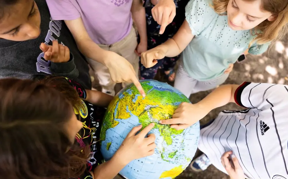 Mehrere Kinder stehen im Kreis und zeigen auf einen Globus.