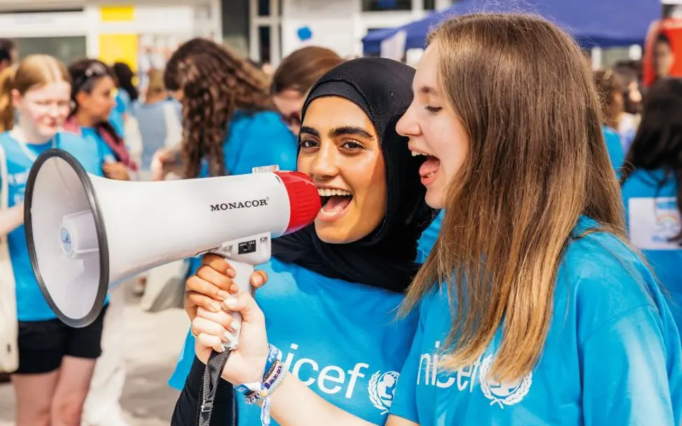 Jugendliche in UNICEF-T-Shirts nutzen ein Megafon bei einem Event draussen.